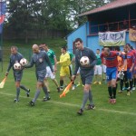Futbalisti Doliny (červené tričká), Cementa a rozhodcovia vystupujú na padinský trávnik v nedeľu
